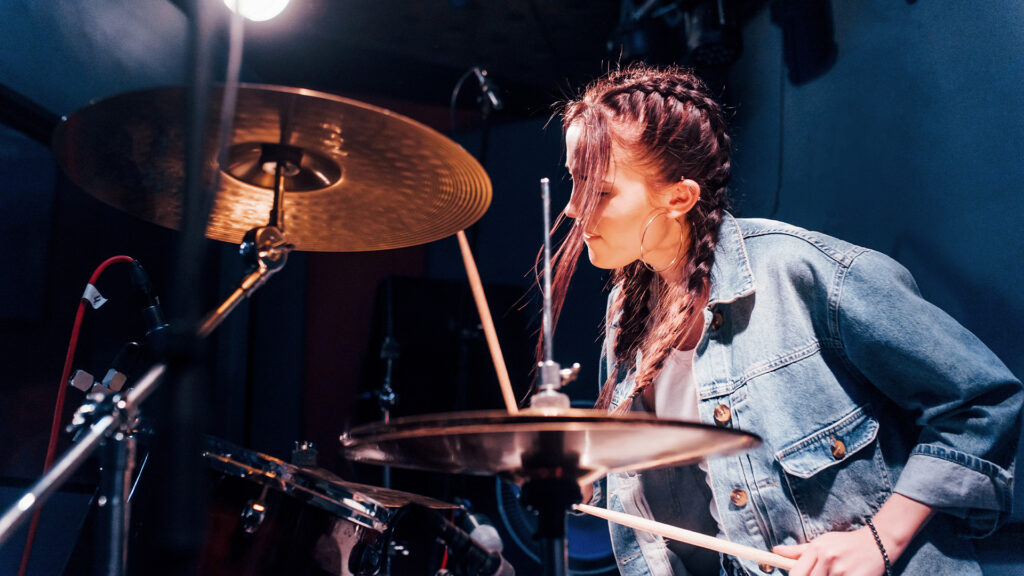 Female performer plays drums, rehearsing in a recording studio